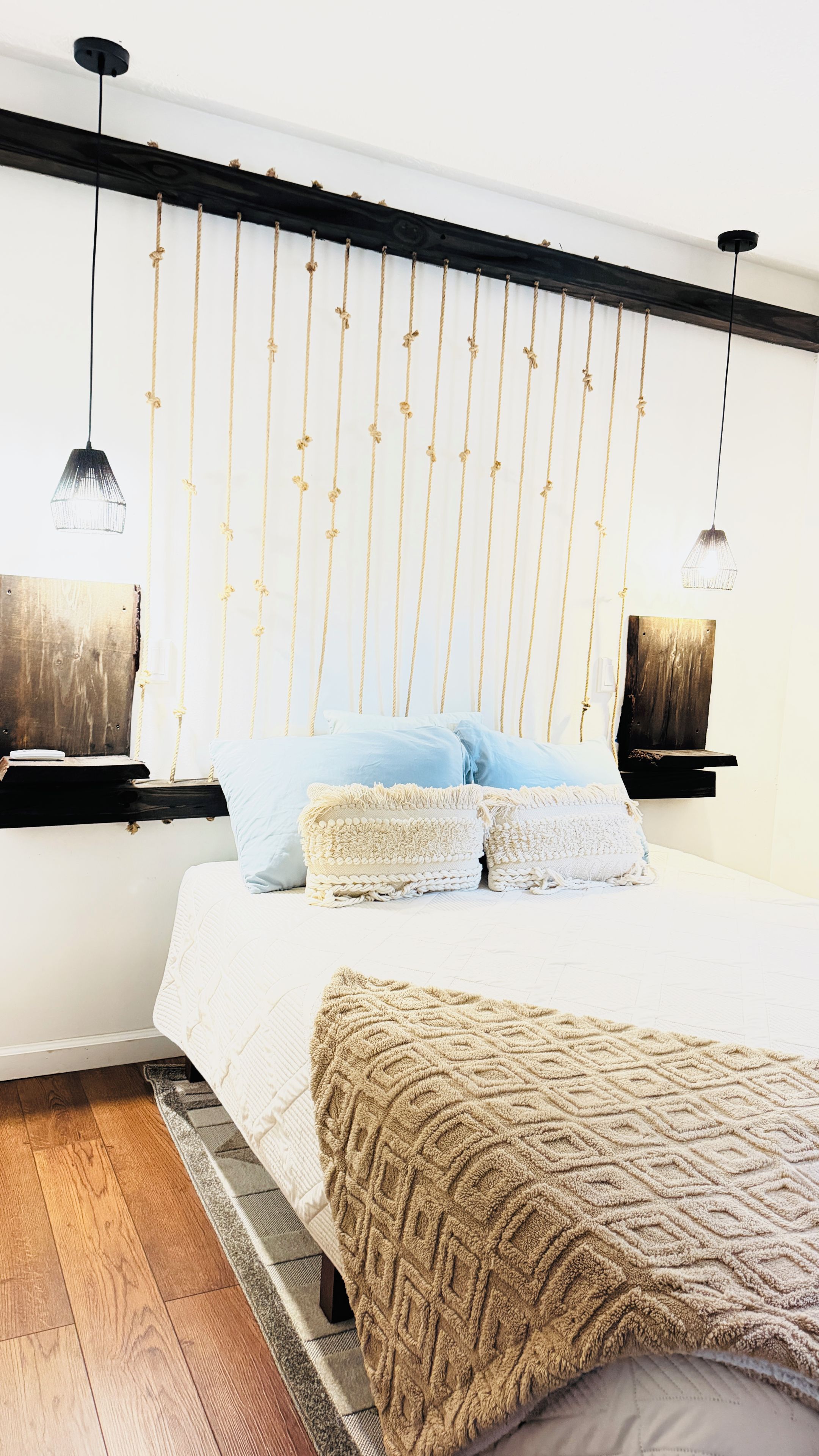 A bedroom with a bed, a wooden headboard, a hanging light fixture, and a bedside table.