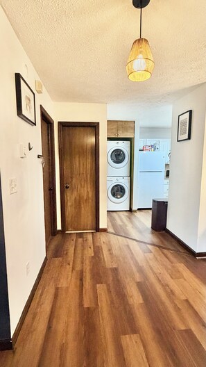 A hallway with wooden flooring leading to a laundry area with a washing machine and dryer. - Arcade + Fire Pit + Pet-Friendly + Pocono Cabin (Tobyhanna)