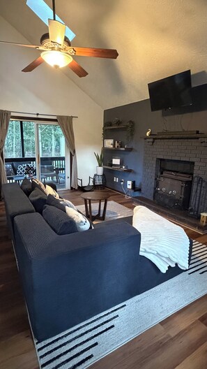 Un salon spacieux avec un canapé aux couleurs sombres, une cheminée et un ventilateur de plafond.