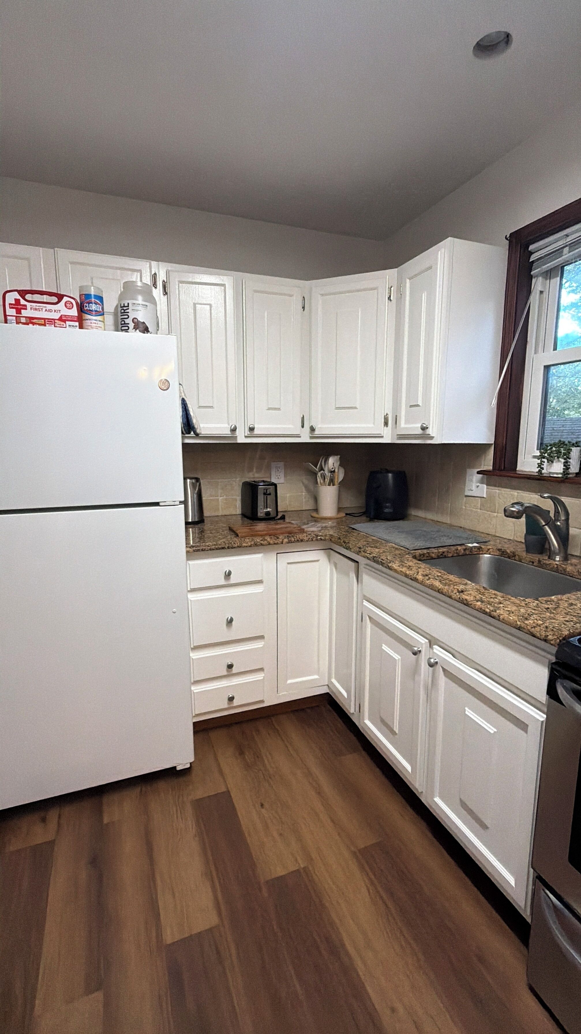 A kitchen with white cabinets, a stainless steel sink, a toaster, and a refrigerator.