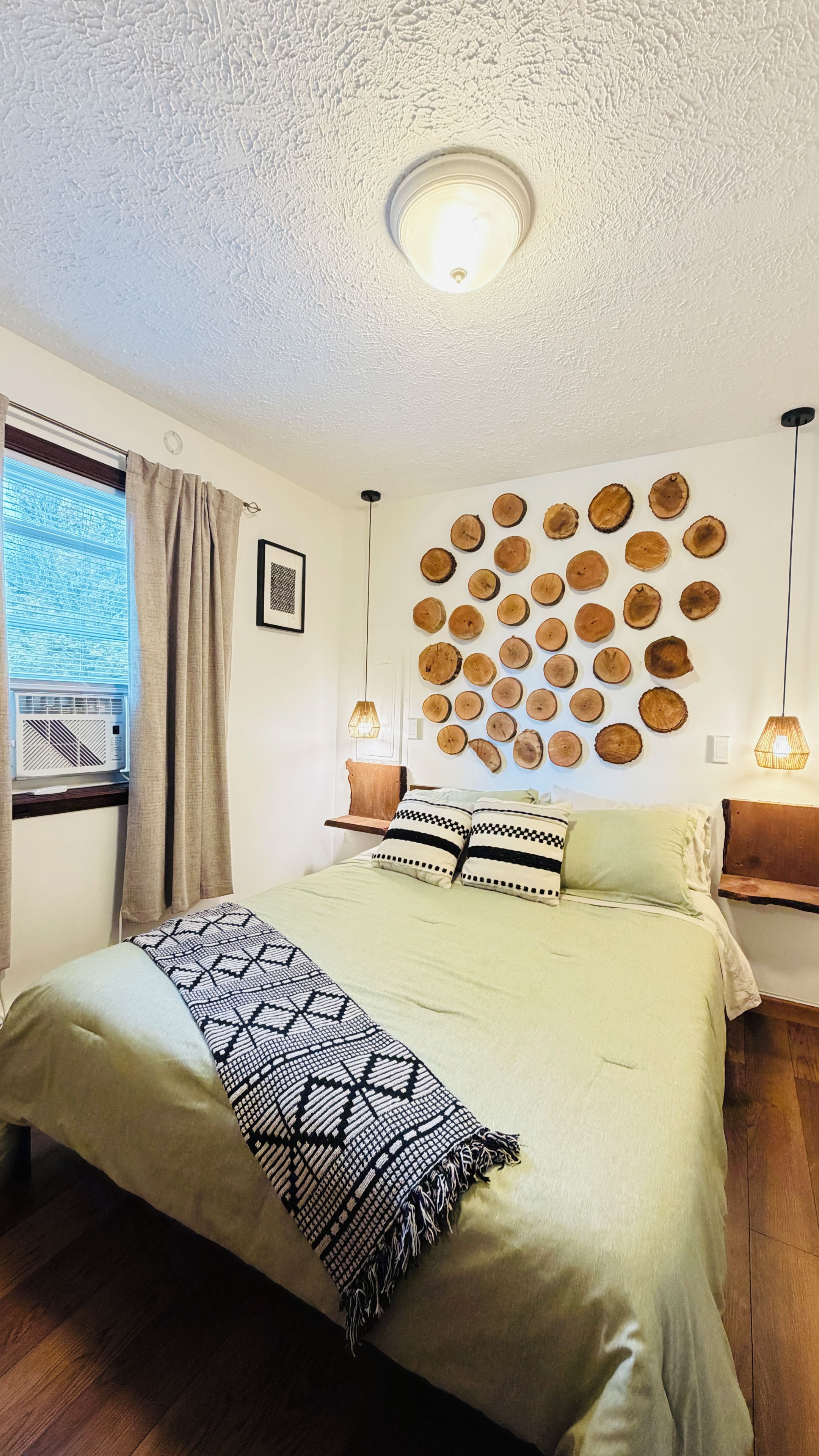 Un dormitorio con cama, una lámpara de pared, una ventana con cortinas y una decoración de rodajas de madera.