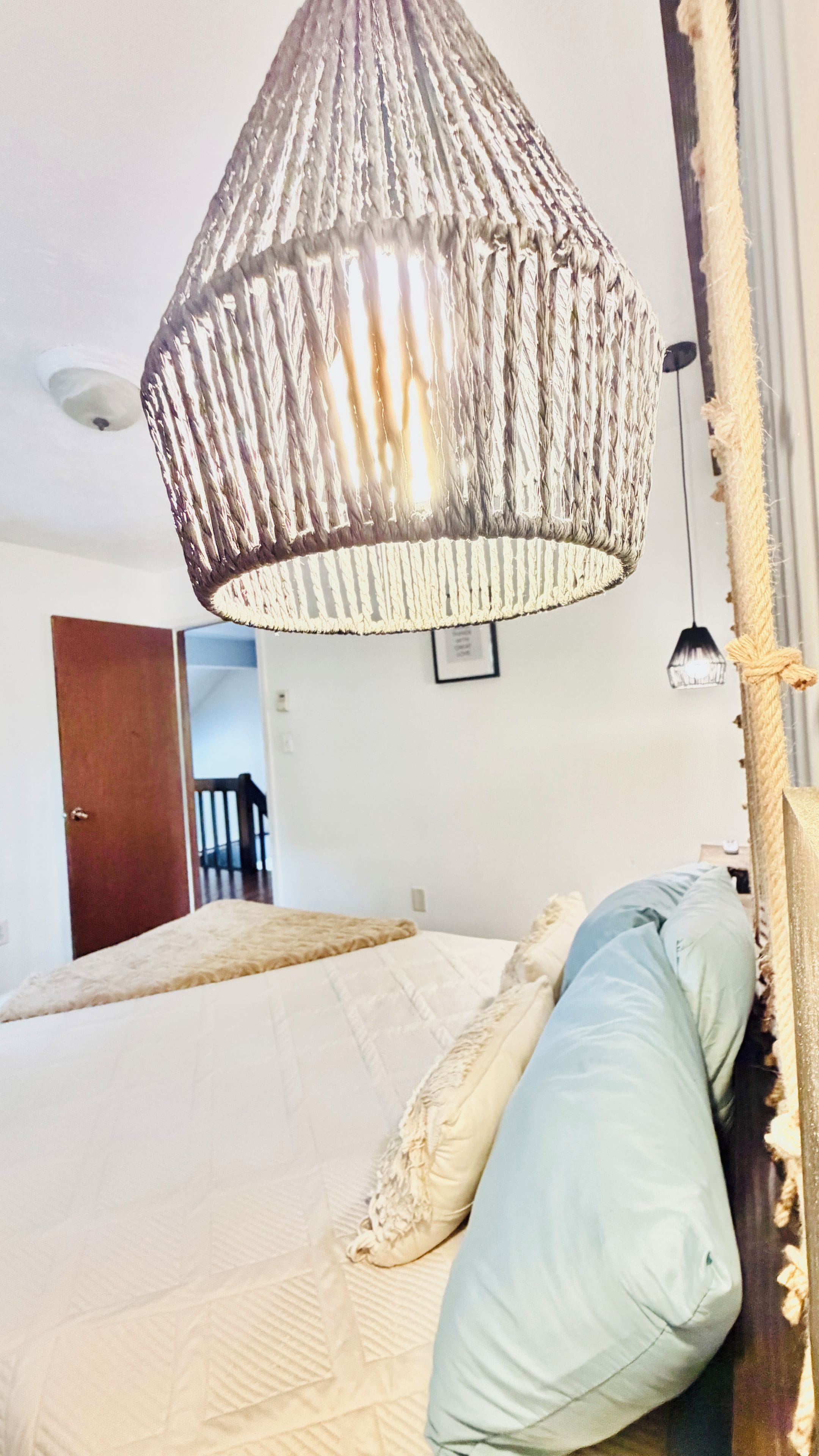 A bed with a textured headboard, a hanging light fixture, and a door in the background.