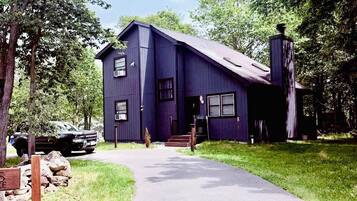 A two-story house with a dark exterior, a chimney, and a paved driveway leading to the entrance.
