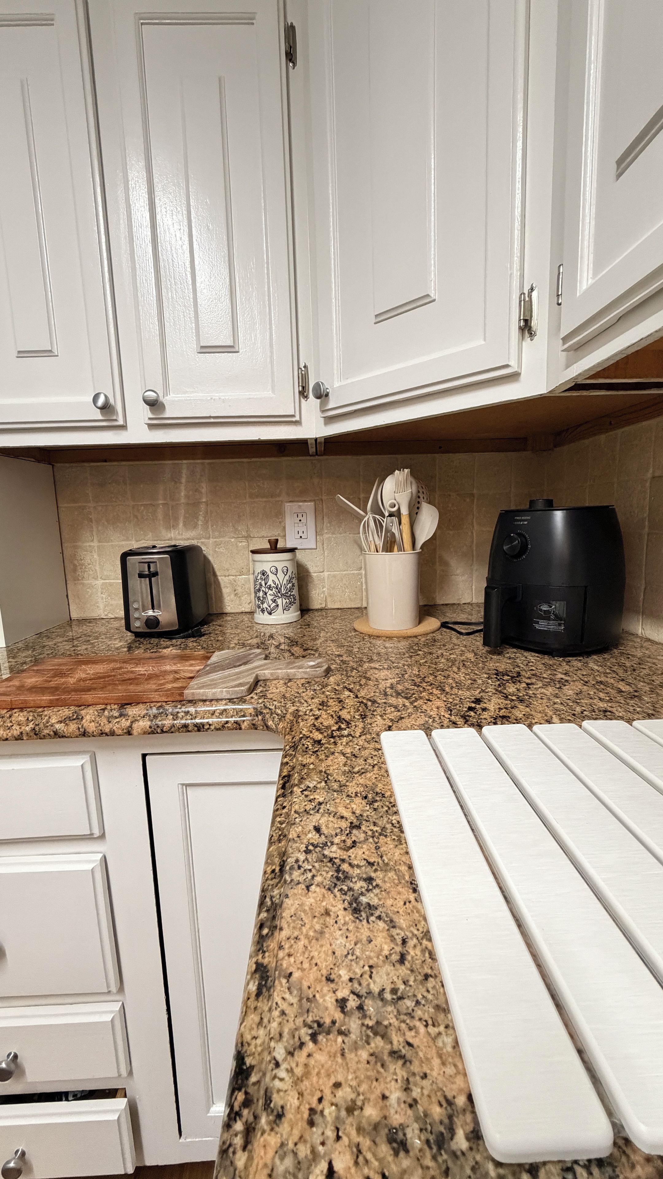 A kitchen with white cabinets, a granite countertop, a toaster, a coffee maker, and a utensil holder.