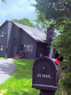 A mailbox with 'US MAIL' written on it, a house in the background, and a clear sky. - Graphite Grove - Arcade, Fire Pit & Covered Deck - Pet Friendly - Poconos (Tobyhanna)