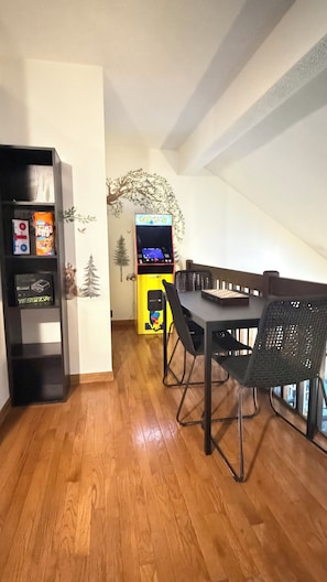 Un coin repas avec une table en bois, des chaises et une borne d’arcade Pac-Man.