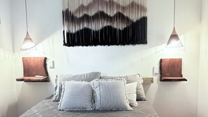 Ein Schlafzimmer mit einem großen Bett, zwei Nachttischen, einem Wandbild und Pendelleuchten.