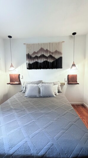 A bedroom with a large bed, two bedside tables, a wall-mounted artwork, and pendant lights. - Graphite Grove - Arcade, Fire Pit & Covered Deck - Pet Friendly - Poconos (Tobyhanna)