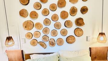 A bedroom with a bed, pillows, a wall-mounted wooden art piece, and pendant lights.
