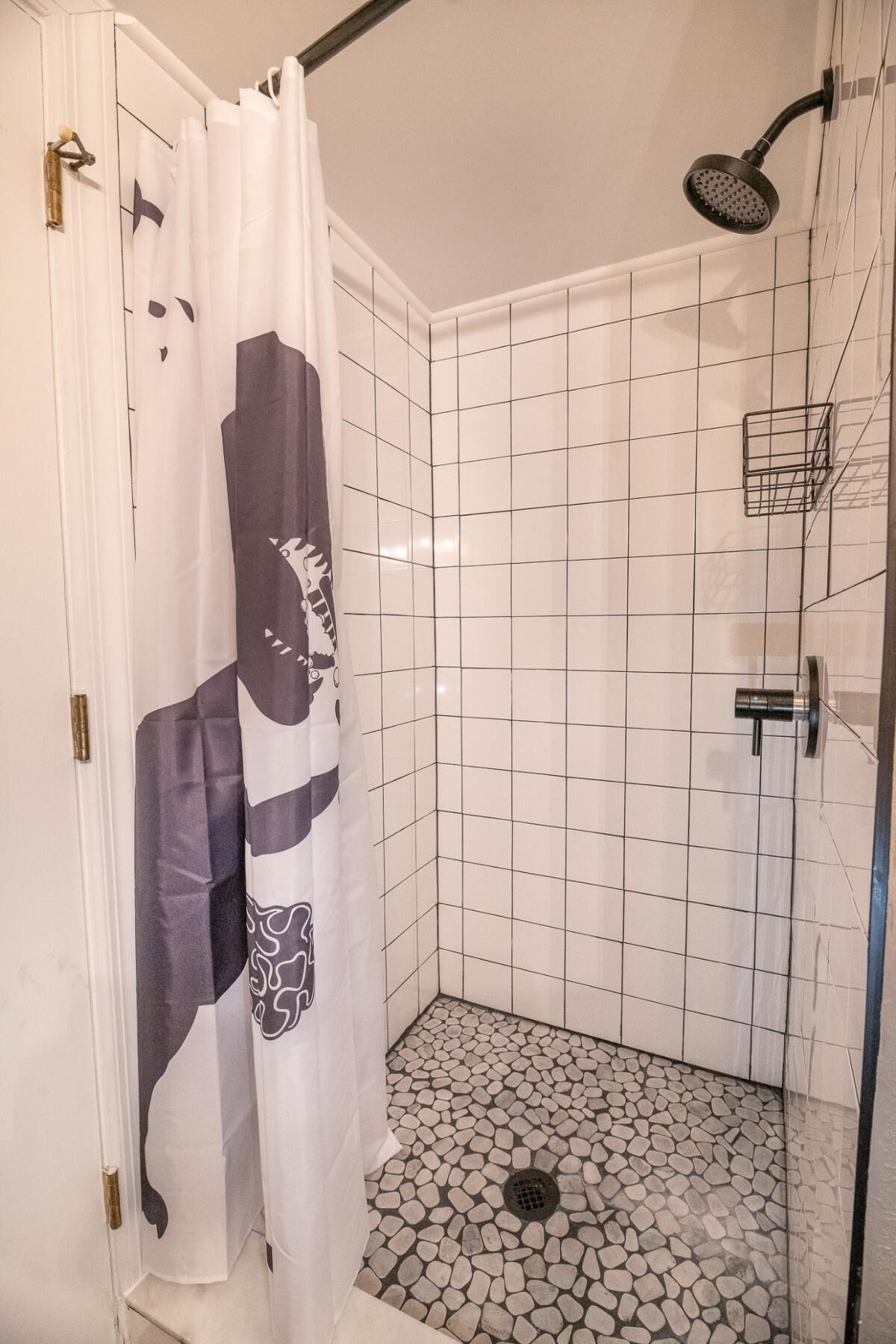 En dusch med ett vitt draperi, kaklade väggar och ett golv med ett mönster som liknar småsten.