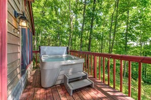 A hot tub on a wooden deck with a red railing, surrounded by a forested area. - Three Little Bears (Gatlinburg)