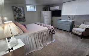 A bedroom with a bed, dresser, TV, and a window.