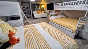 Un dormitorio con literas, una cuna blanca, un peluche y una alfombra estampada.