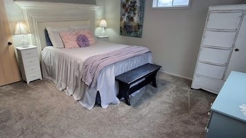 A bedroom with a bed, bedside lamps, a bench, a dresser, and a painting on the wall.