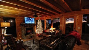 L’intérieur d’un chalet confortable en bois, avec une cheminée, un sapin de Noël et un téléviseur fixé au mur.