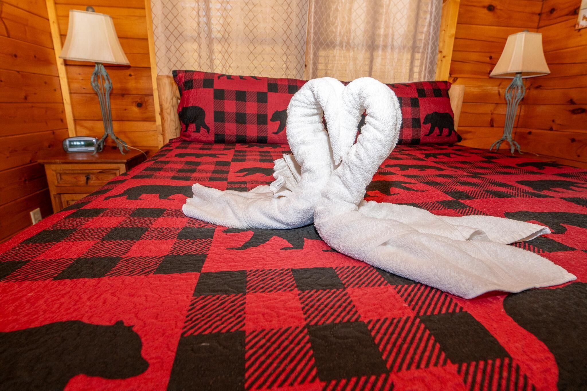 A bed with a red and black checkered bedspread, two nightstands with lamps, and a clock on one of the nightstands.