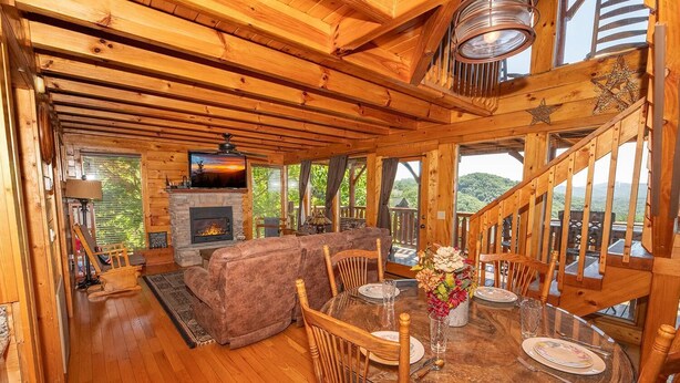 L’intérieur d’un chalet en bois comprend une cheminée, un canapé, une table à manger avec des chaises et un escalier.