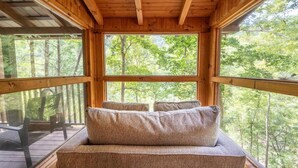 Una cabaña de madera con un ventanal grande, un banco acolchado y vistas a un bosque.