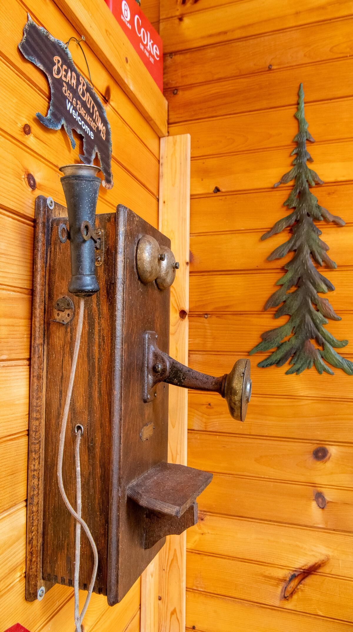 A vintage-style doorbell with a bear-shaped sign above it, a Coke sign, and a Christmas tree decoration on the wall.