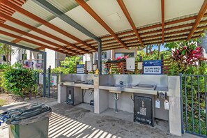 An outdoor barbecue area with a clean-up station, surrounded by greenery and a covered shelter. - Bluewater Duo—Lagoon Views & Pool by Trinity Beach (Trinity Beach)