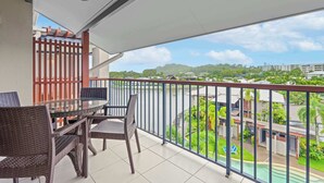 Ein Balkon mit Glastisch und Korbstühlen, einem roten Zaun und Blick auf eine Wohngegend mit Grünflächen und Gebäuden.