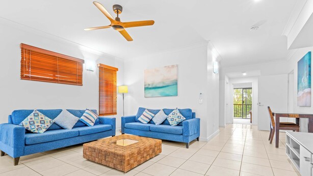 Ein Wohnzimmer mit zwei blauen Sofas, einem Holztisch, einem Deckenventilator und Blick ins Freie.