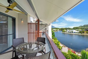 A balcony with a glass table and chairs, overlooking a body of water and a mountainous landscape. - Bluewater Duo—Lagoon Views & Pool by Trinity Beach (Trinity Beach)