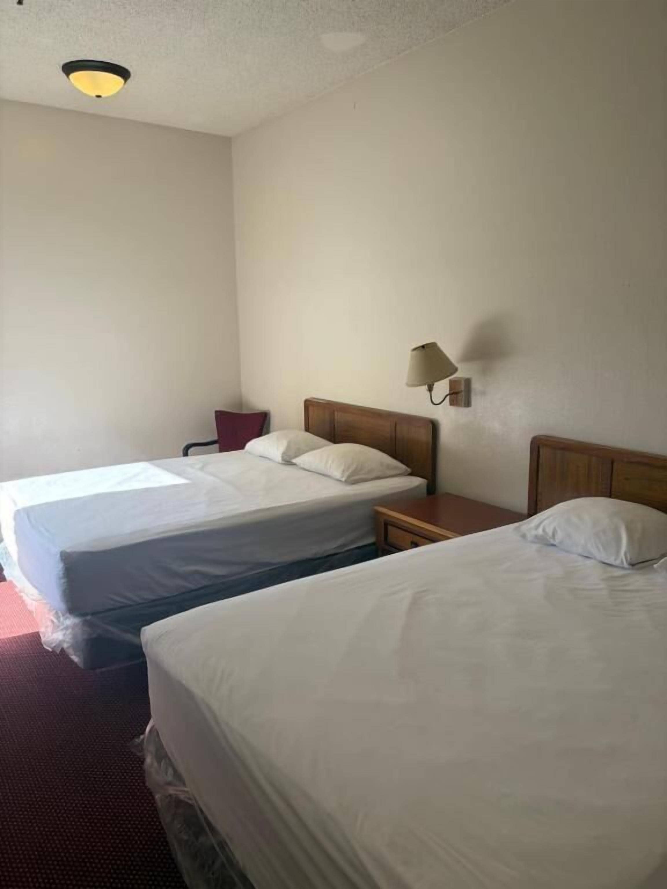 A hotel room with two single beds, a nightstand, a lamp, and a ceiling light.