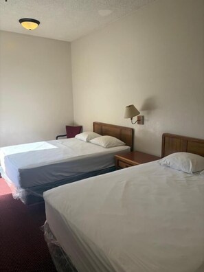 Habitación de hotel con dos camas individuales, una mesita de noche, una lámpara y una luz en el techo.