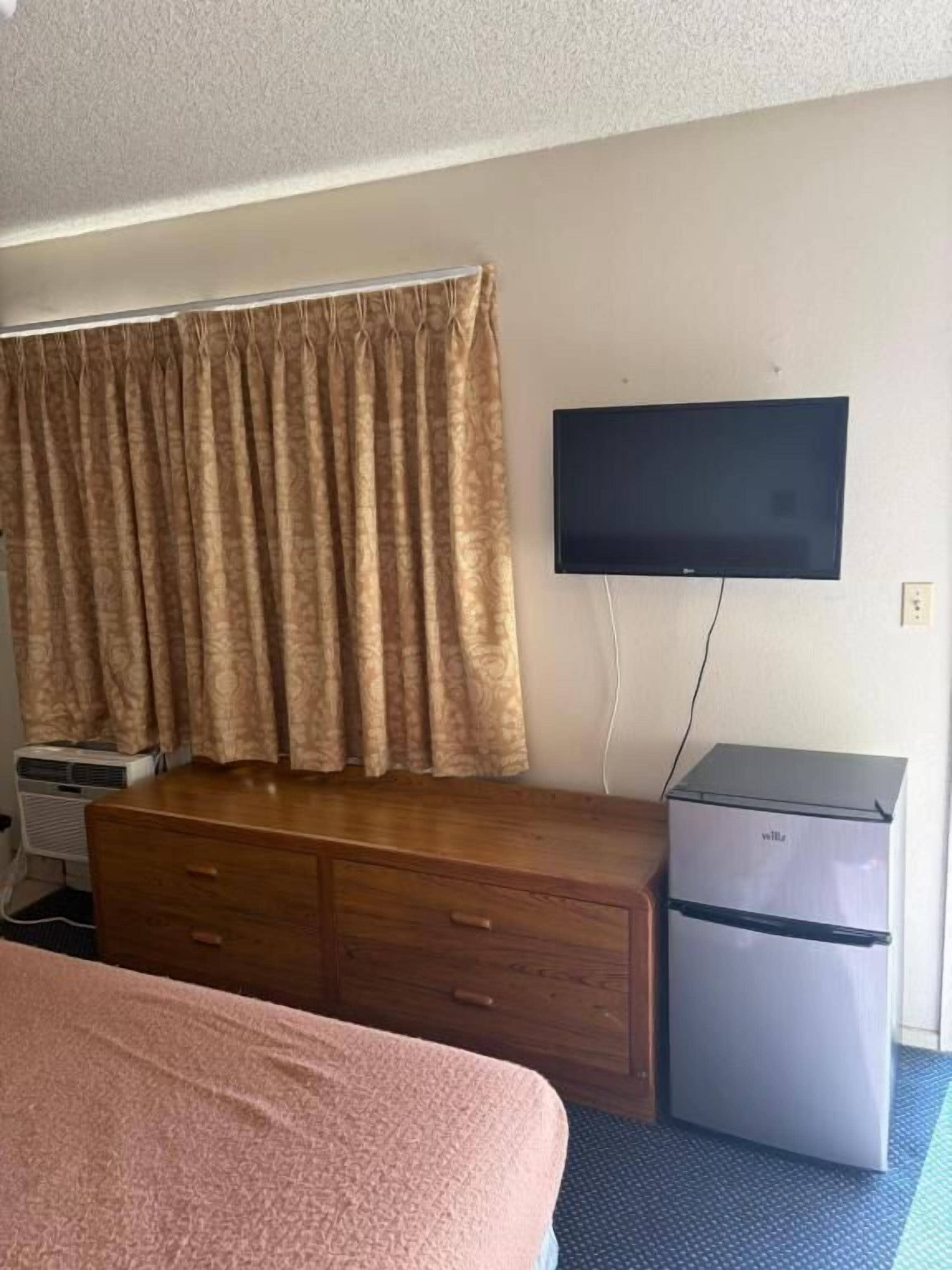 Una stanza con un letto, una cassettiera, una televisione montata a parete e un frigorifero.