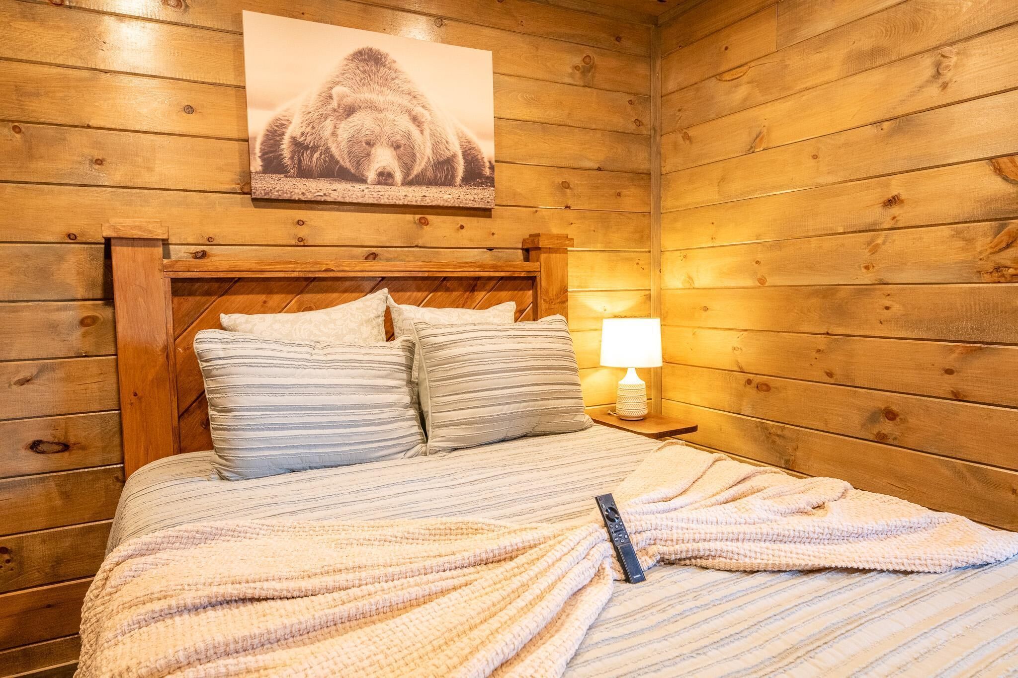 Habitación de cabaña de madera con cama, almohadas, una colcha, un control remoto y un cuadro en la pared.