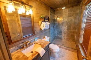 A modern bathroom with a wooden vanity, a glass shower enclosure, and a framed picture on the wall. - Amazing Grace (Sevierville)