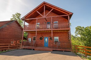A two-story log cabin with a balcony, a front door, and a small porch area. - Amazing Grace (Sevierville)