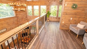L’intérieur d’un chalet en bois, avec un escalier, un canapé gris et un luminaire suspendu.