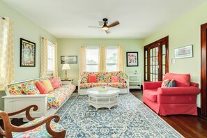 A living room with a sofa, armchair, and coffee table, a patterned rug, and a ceiling fan. - Blue Turtle - Vintage Island Charm in Midtown (Galveston)