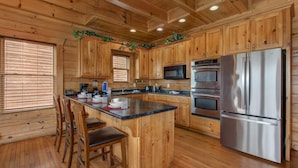 A wooden cabin interior with a kitchen featuring wooden cabinets, a central island with bar stools, a stainless steel refrigerator, and built-in appliances. - Splash Mountain (Sevierville)