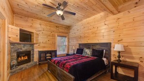 A wooden cabin bedroom with a bed, a fireplace, a ceiling fan, and a window. - Splash Mountain (Sevierville)