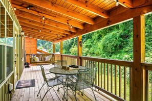 A covered outdoor deck with a table and chairs, wooden railings, and a view of a forested area. - Duck Duck Moose (Sevierville)