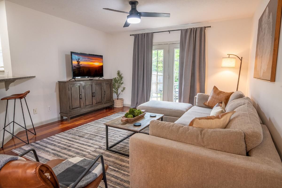 A living room with a sofa, a coffee table, a TV, a ceiling fan, and a window with curtains.
