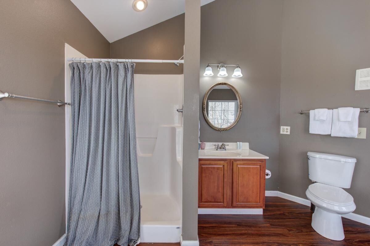 A bathroom with a shower, toilet, vanity, and a mirror.
