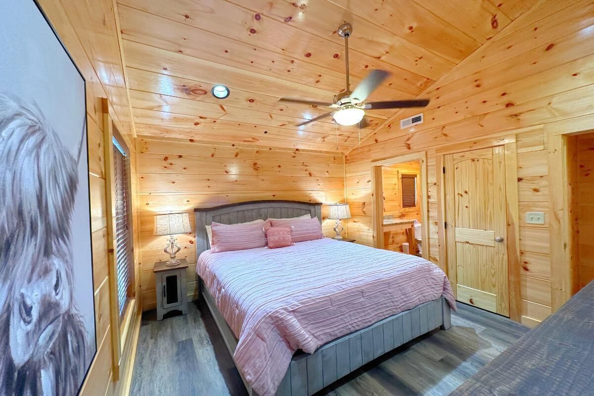 A wooden cabin bedroom with a bed, a ceiling fan, a nightstand, and a door.