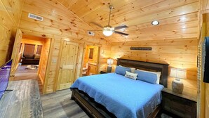 A wooden cabin bedroom with a bed, ceiling fan, and a sign on the wall. - Shepherd's Rest (Pigeon Forge)