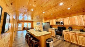 A wooden cabin interior with a kitchen, dining area, and bar stools. - Shepherd's Rest (Pigeon Forge)