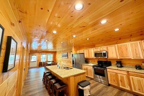 A wooden cabin interior with a kitchen, dining area, and bar stools. - Shepherd's Rest (Pigeon Forge)