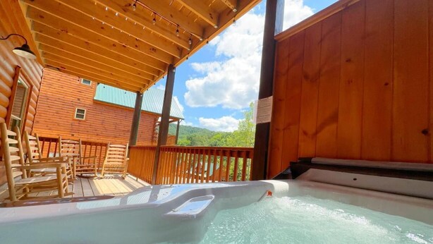 A hot tub area with wooden deck seating and a view of a mountain. - Shepherd's Rest (Pigeon Forge)