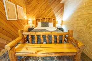 Ein Schlafzimmer einer Holzhütte mit einem Bett, einer Holzbank und zwei gerahmten Bildern an der Wand.