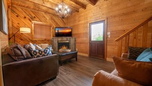 A cozy cabin interior with a fireplace, wooden walls, a sofa, and a television. - Big Bear Lodge at Valley View (Sevierville)