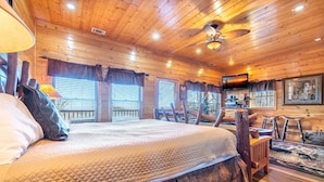 A wooden cabin interior with a large bed, a television, and a dining area. - Smokey's Hideaway (Sevierville)