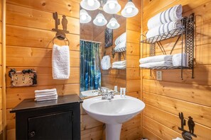 A wooden cabin bathroom with a sink, towel rack, and shelves for towels. - Smokey's Hideaway (Sevierville)