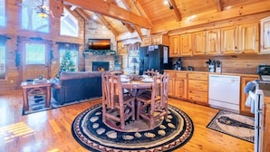 A log cabin interior with a dining area, kitchen, and fireplace. - Smokey's Hideaway (Sevierville)
